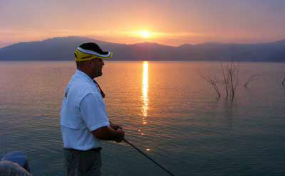 Sun sets on an angler fishing thorn trees on giant bass Mexican bass lake Comedero. Sun sets on an angler fishing thorn trees on giant bass Mexican bass lake Comedero.