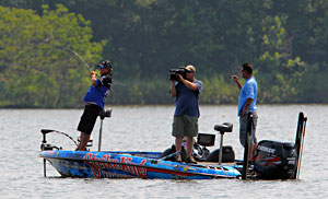 Legendary bass pro Denny Brauer maintains a strong lead on day three of the 2011 Elite Series Diamond Drive on the Arkansas River hooking a bass in front of Mark Zona and cameraman James Massey Legendary bass pro Denny Brauer maintains a strong lead on day three of the 2011 Elite Series Diamond Drive on the Arkansas River hooking a bass in front of Mark Zona and cameraman James Massey